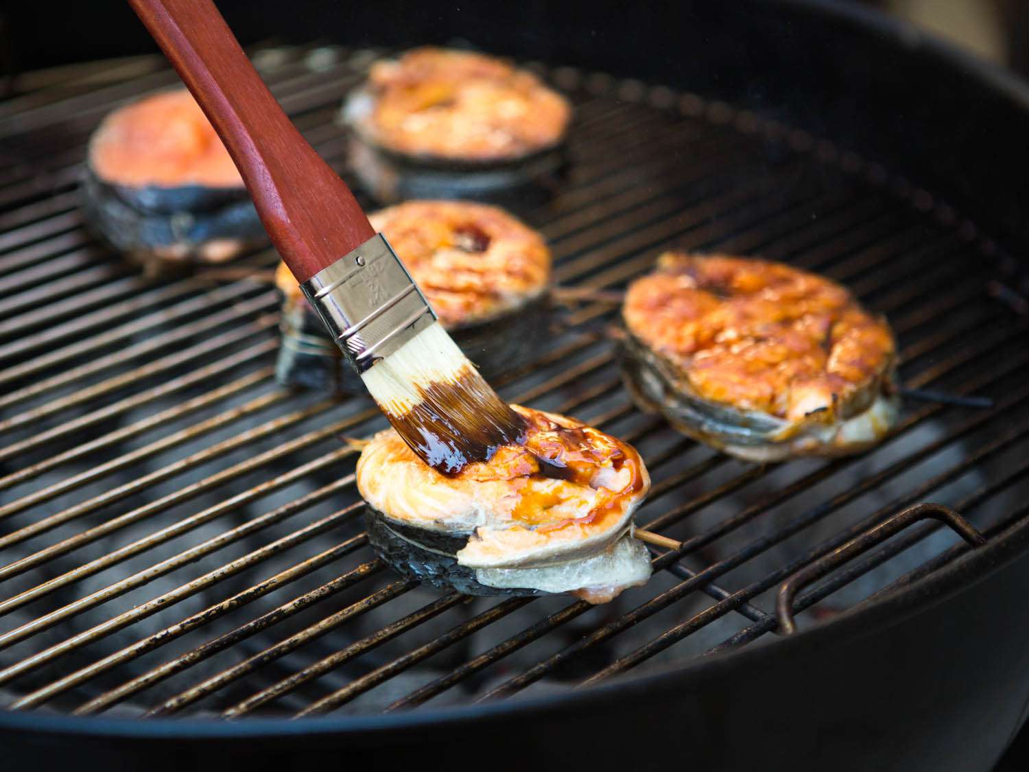 Brushing teriyaki sauce on grilled salmon steaks.