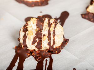A chocolate-drizzled coconut macaroon on parchment paper.