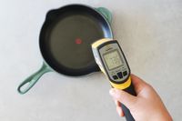A person pointing an infrared thermometer at an enameled cast iron skillet.