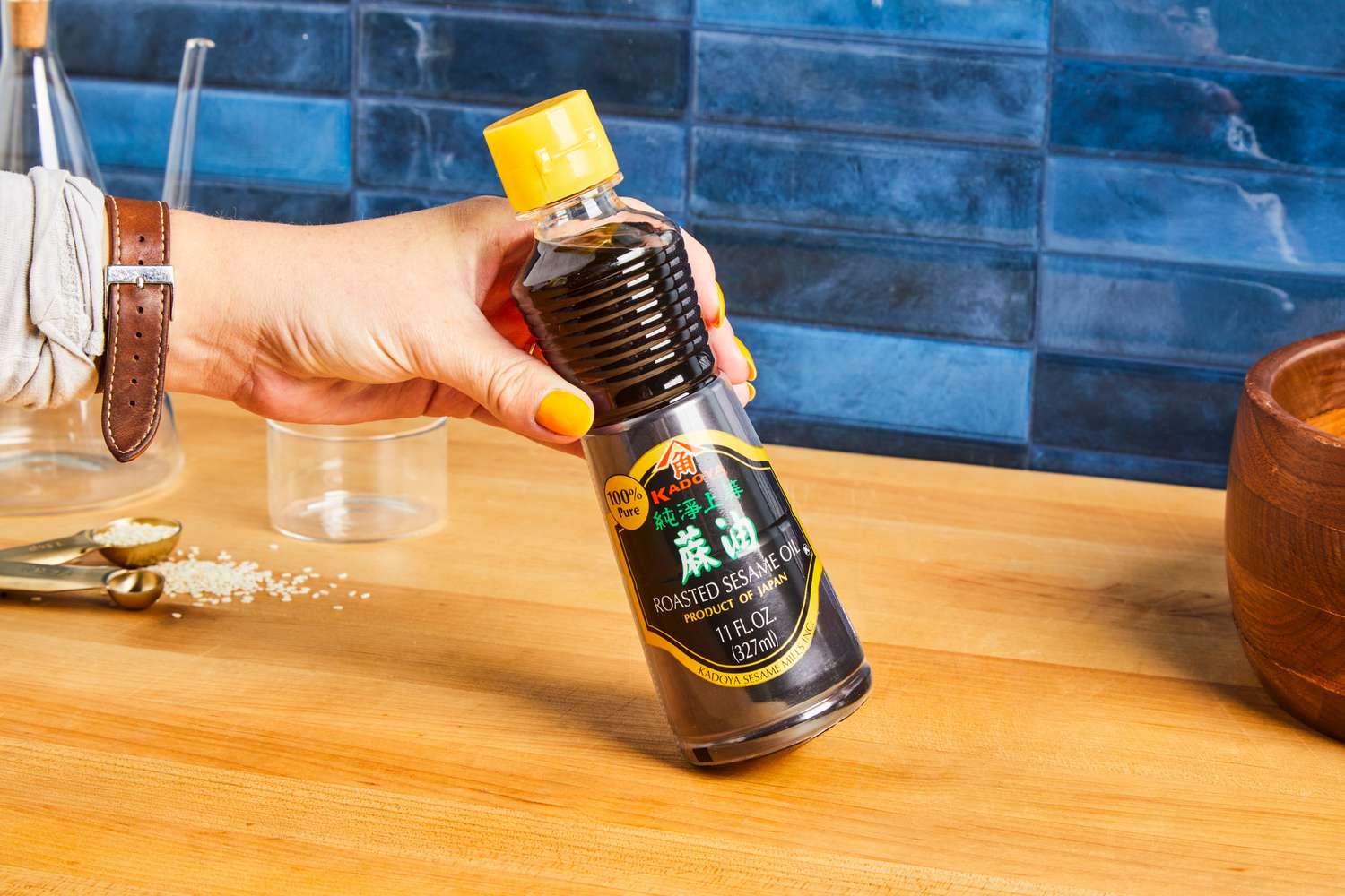 A hand holding a bottle of Kadoya brand pure sesame oil against a kitchen countertop