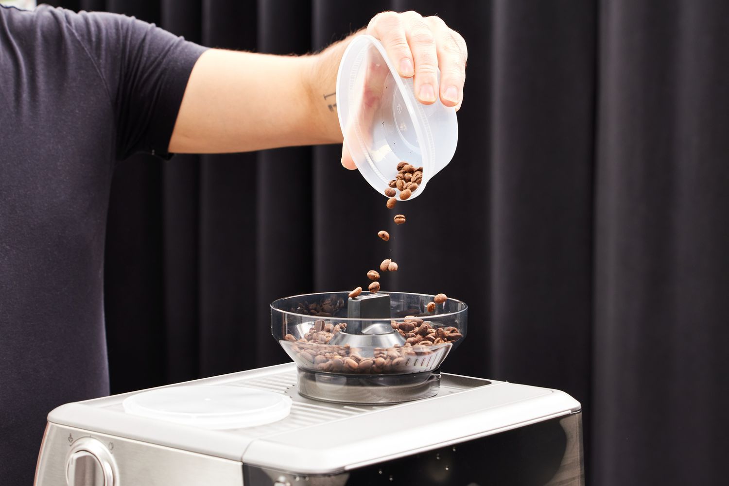 A person pouring in coffee beans into the coffee griner part of the Breville Barista Express Impress