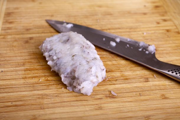 A ball of finely chopped shrimp on a cutting board, with a knife next to it.