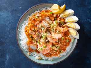 Overhead view of pancit palabok, served on an earthenware platter and garnished with lemon wedges and a quartered hard-boiled egg.