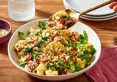A dish of roasted cauliflower with grapes herbs and nuts being scooped with a spoon