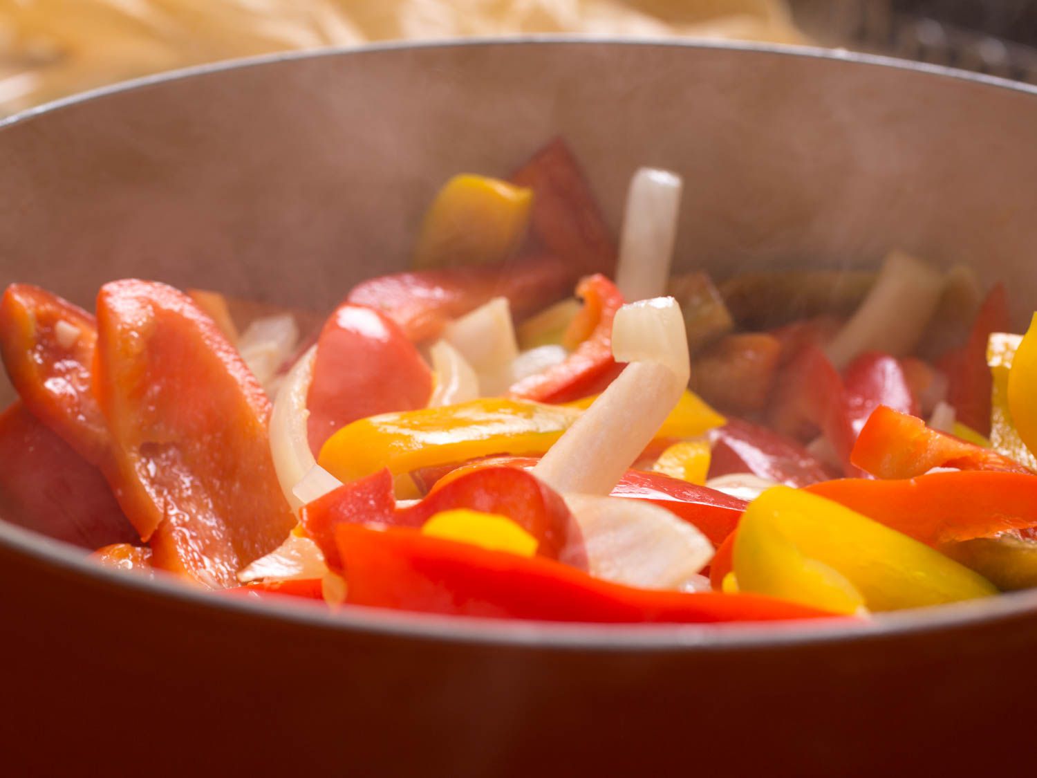 Sauteing sliced onions, red and yellow bell peppers.