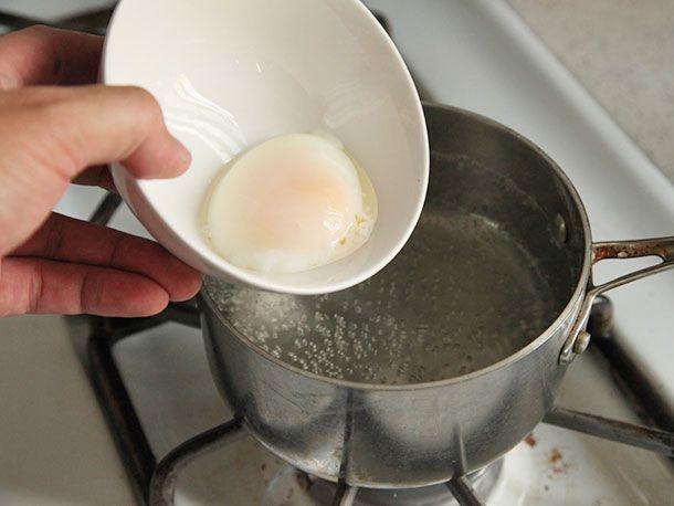 Sous vide poached egg in bowl about to be placed in pot of simmering water