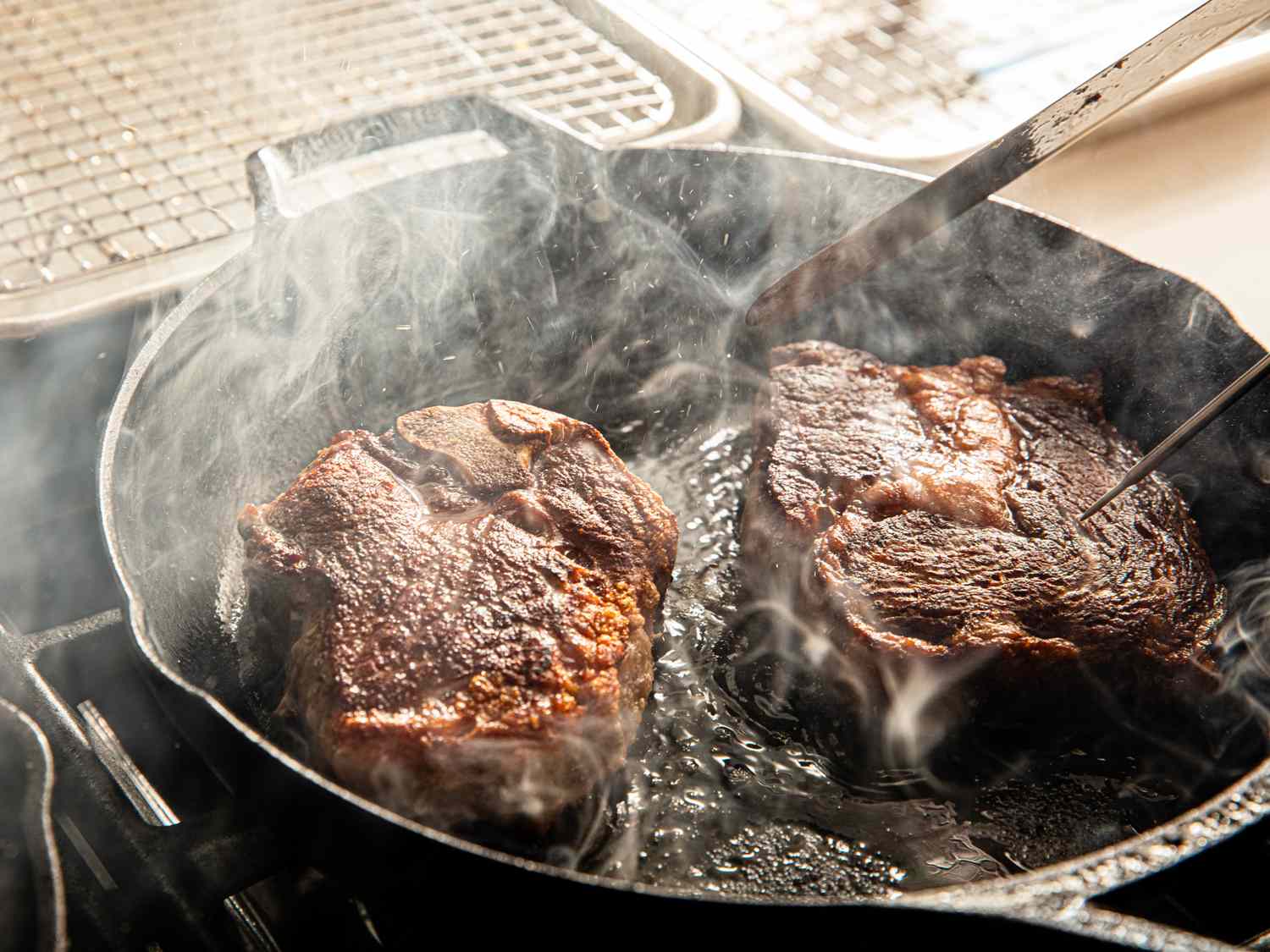 Two steaks cooking in a cast iron skillet with steam rising up