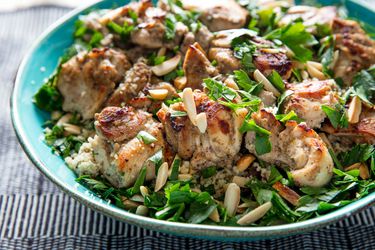 Broiled tandoori chicken, served in a blue bowl over couscous and garnished with slicered almonds and herbs.