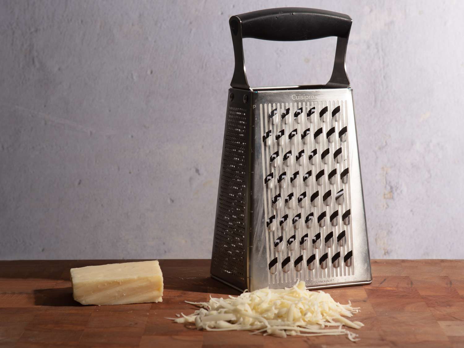 A box grater with a hunk of cheese beside it