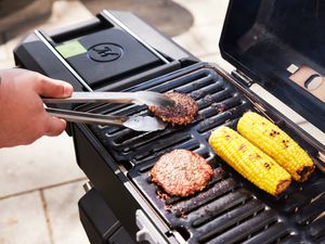 A person cooking burgers and corn on the cob on the Masterbuilt portable charcoal grill.