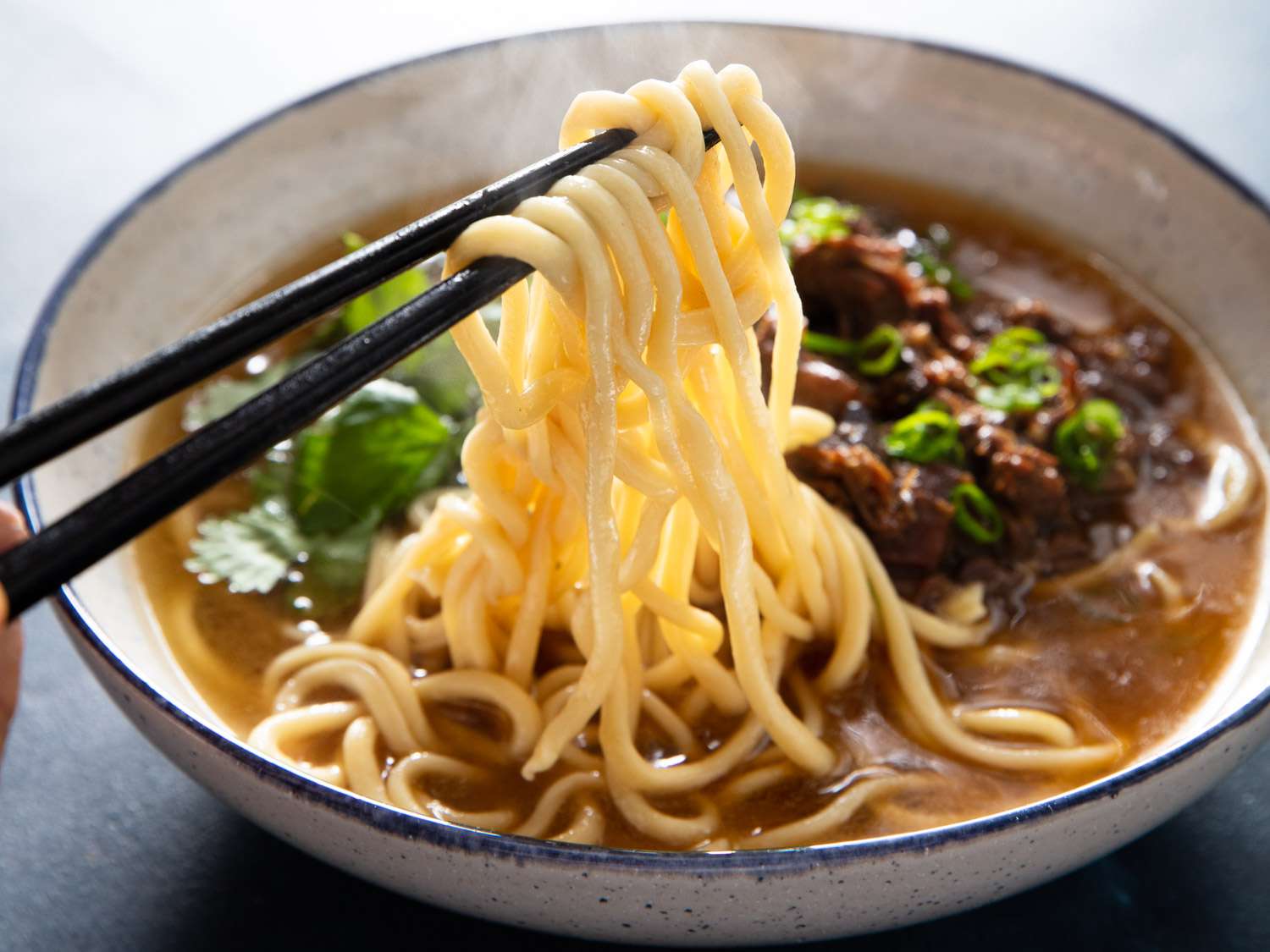 Hand-pulled noodles being pulled out of a bowl of lamb soup with chopsticks.