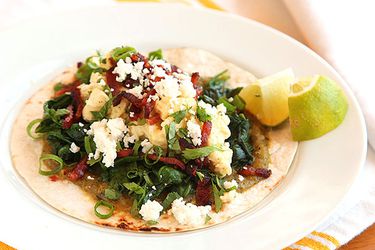 A plate of breakfast tacos with scrambled eggs, spinach, bacon, and crumbled cotija.