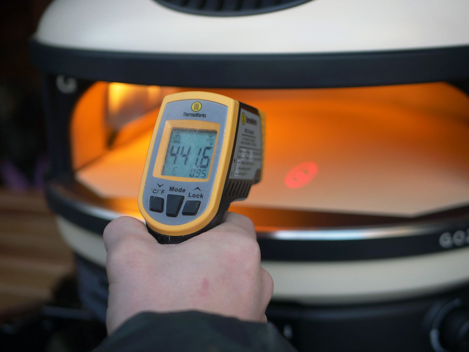a person holding an infrared thermometer and pointing it at the center of the pizza stone inside the Gozney arc