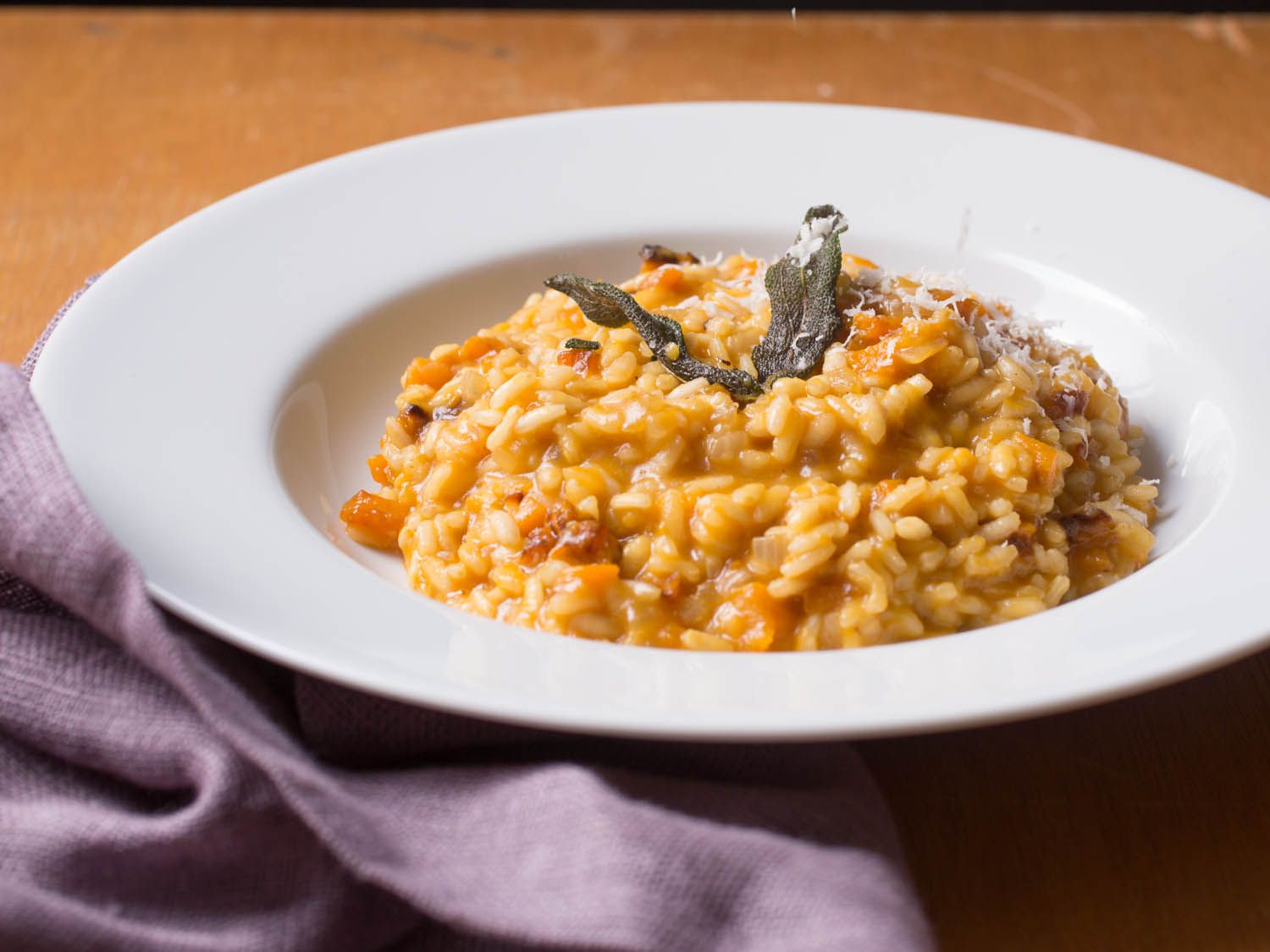 Side view of a plate of butternut squash risotto, topped with grated cheese and fried sage leaves.