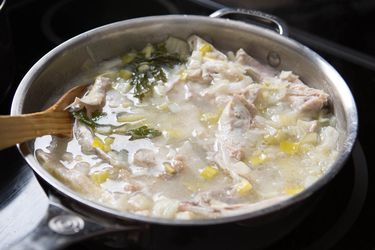 A wooden spoon stirring a large pot of fish stock.