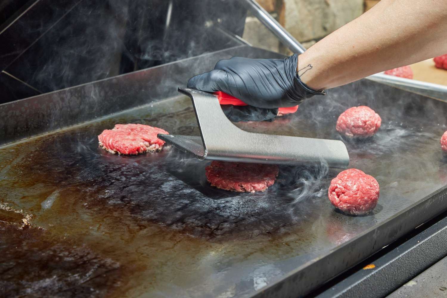 A person makes smashburgers on the Weber Slate 30 Inch Griddle