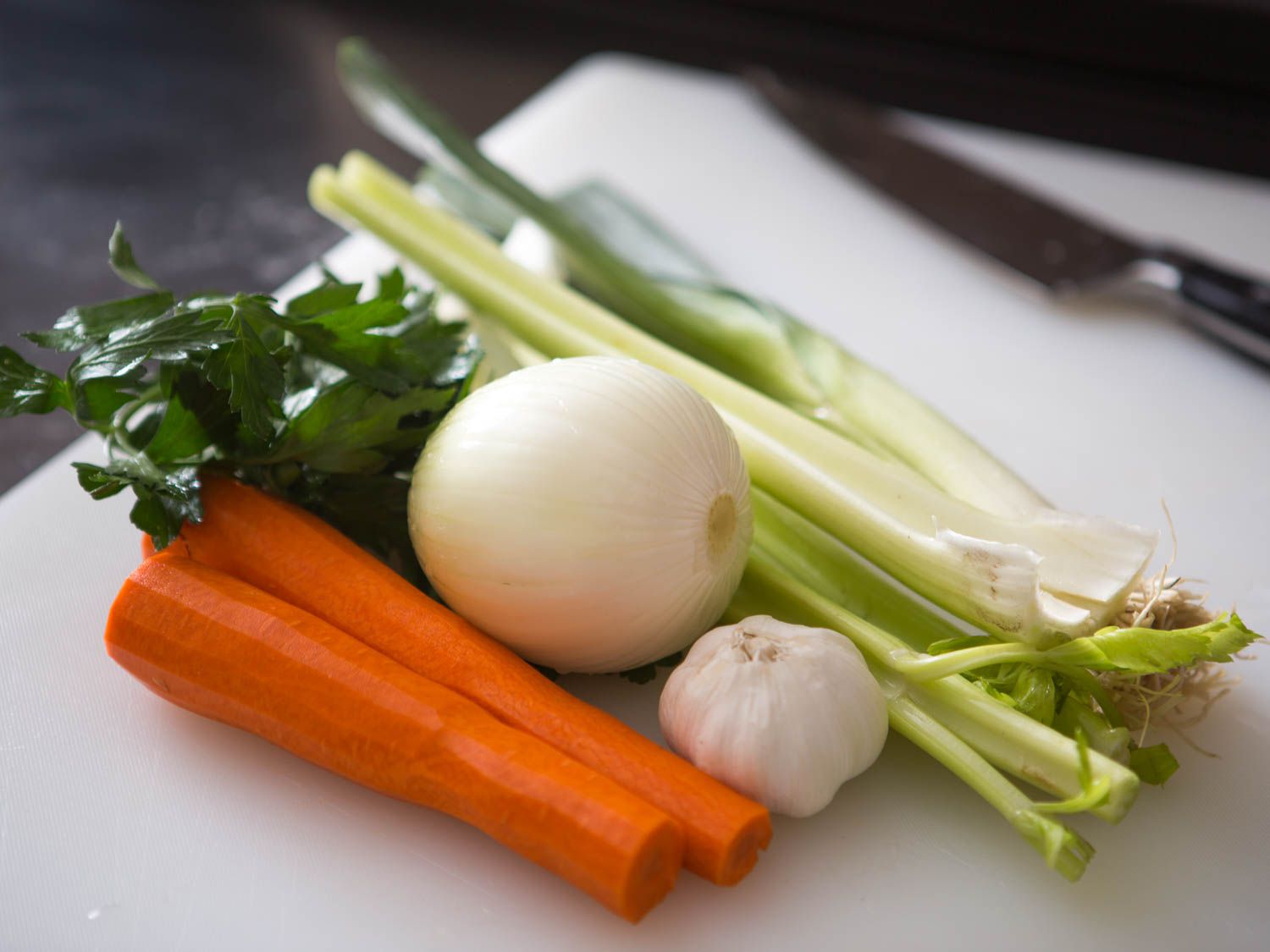 Ingredients for vegetable stock on a cutting board: carrots, onion, galic, celery, and parsley. 