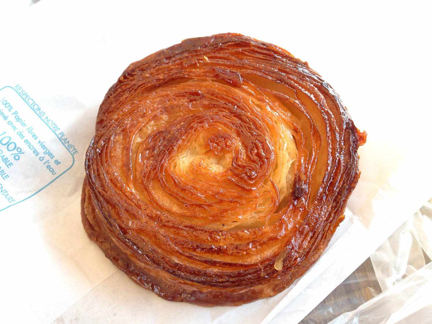 Overhead photo of kouign amann pastry on top of white paper bag.