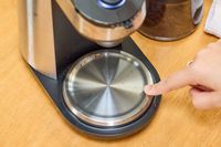 A person touches the OXO Brew Conical Burr Coffee Grinder With Integrated Scale