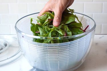 a person placing mixed greens into a salad spinner