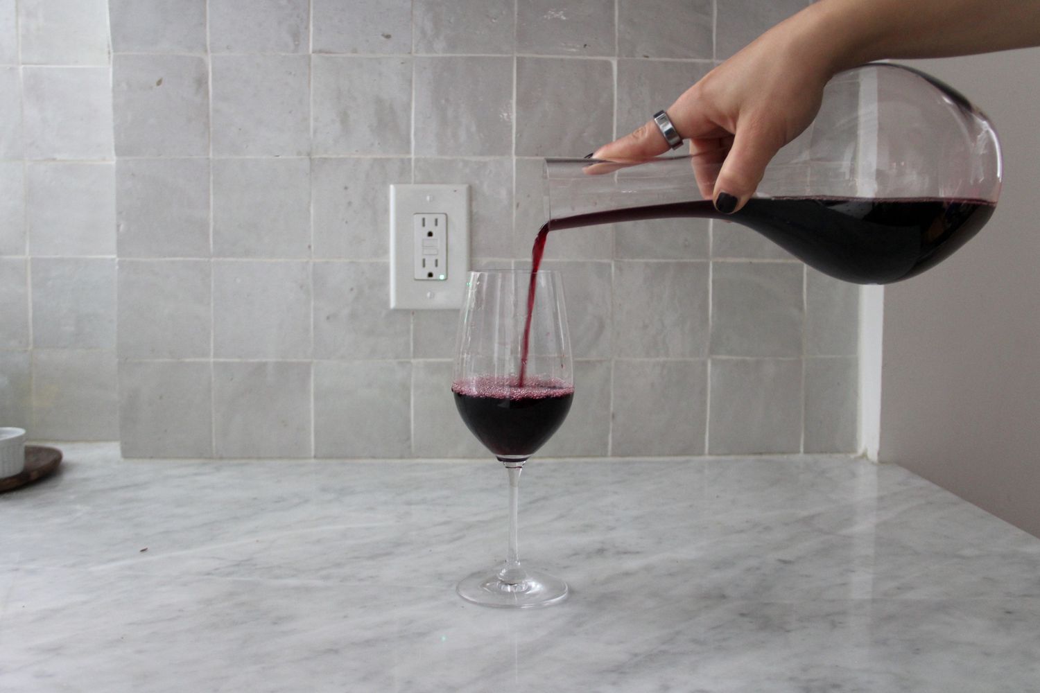 A person pouring red wine from the Glasvin decanter into a wine glass