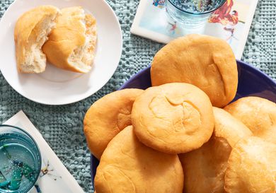 Overhead angle of Platter of Johnny Cakes on a blue platter, with a cake on a smaller plate in front, ripped open. 2 glasses of sparkling water and blue tablecloth 
