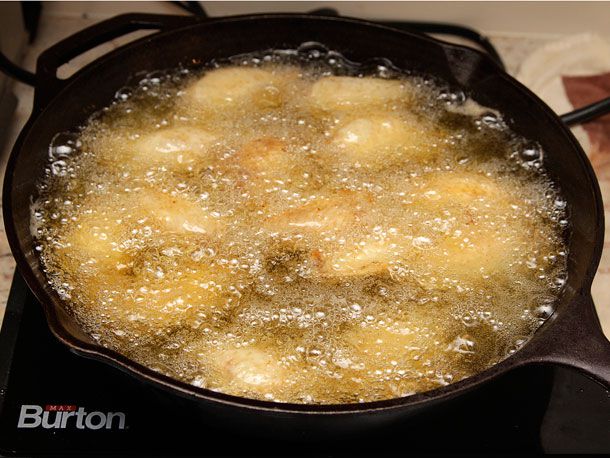Buffalo wings frying in a cast iron pan.