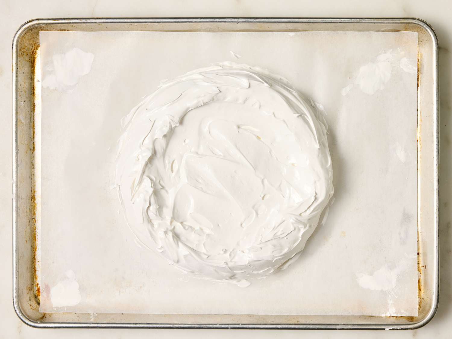Unbaked meringue spread into a circular shape on a baking sheet lined with parchment paper