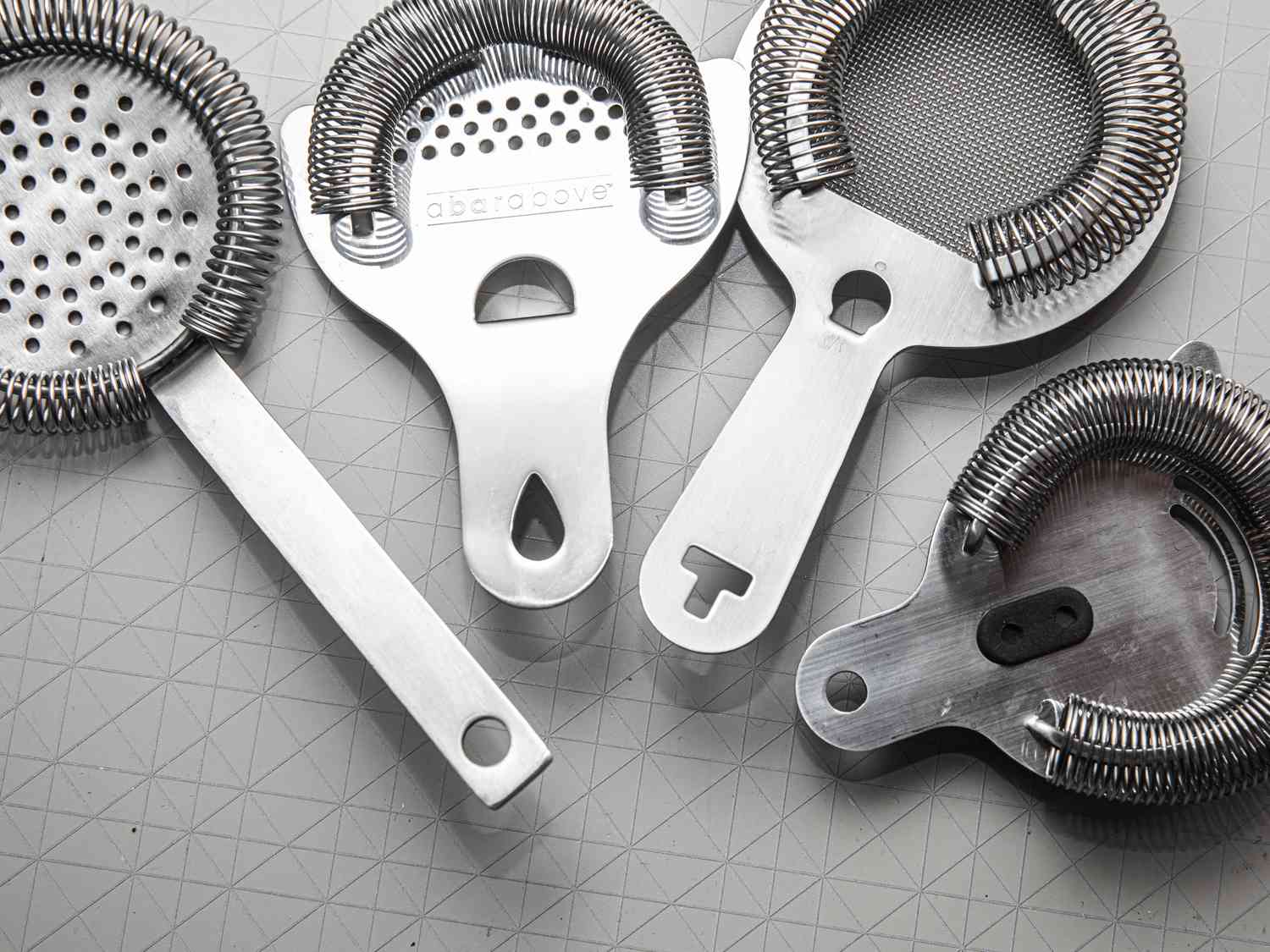 Four different hawthorne strainers with various handle lengths on a grey surface