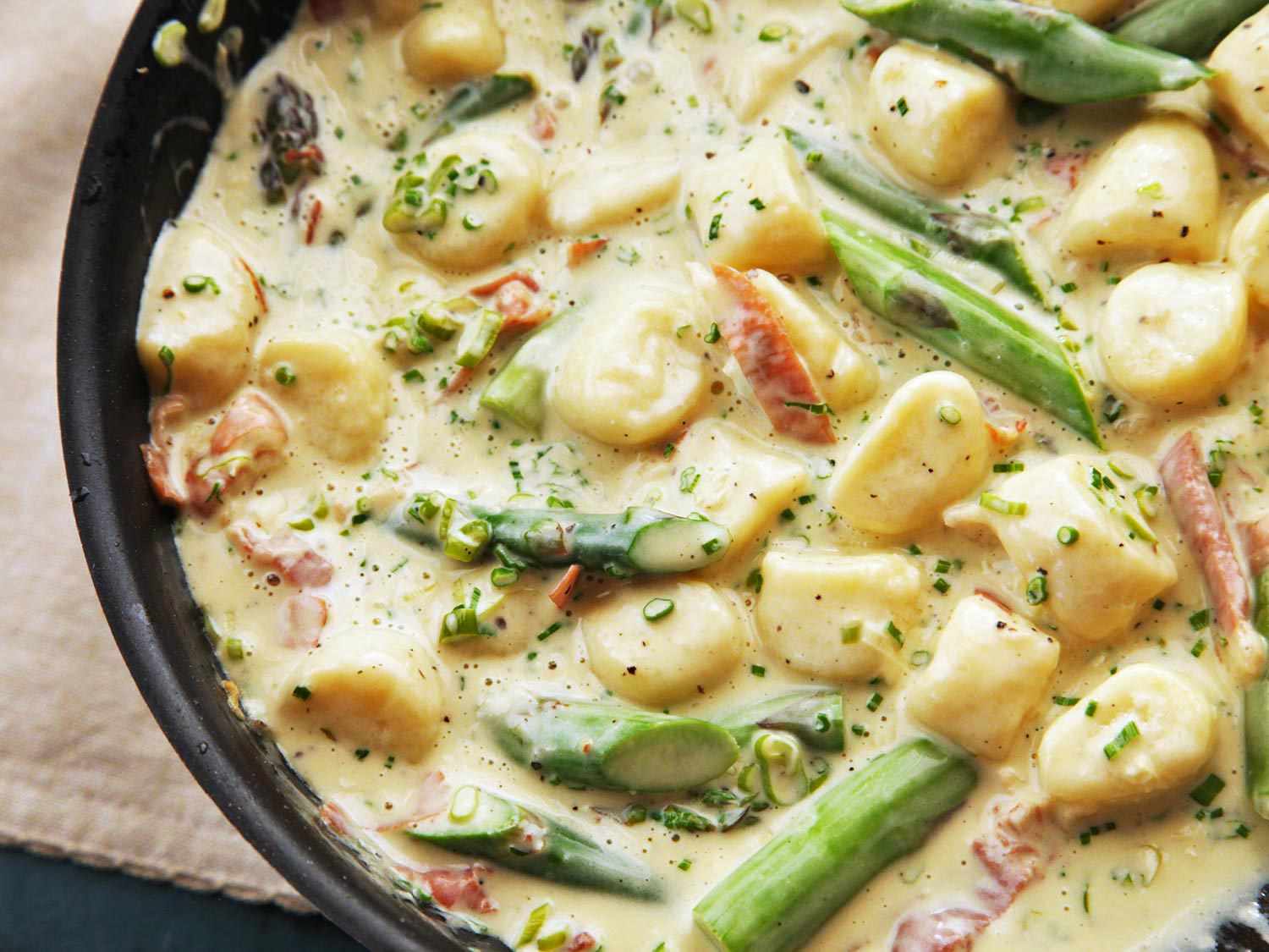 A skillet of homemade ricotta gnocchi with a creamy prosciutto and asparagus sauce.