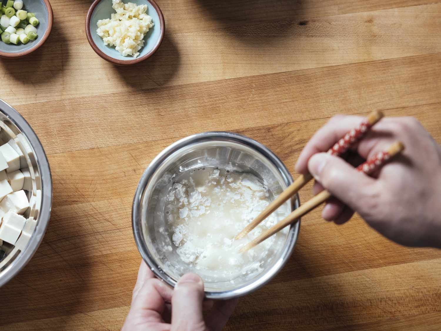 Cornstarch slurry being mixed in a metal bowl with chopsticks.