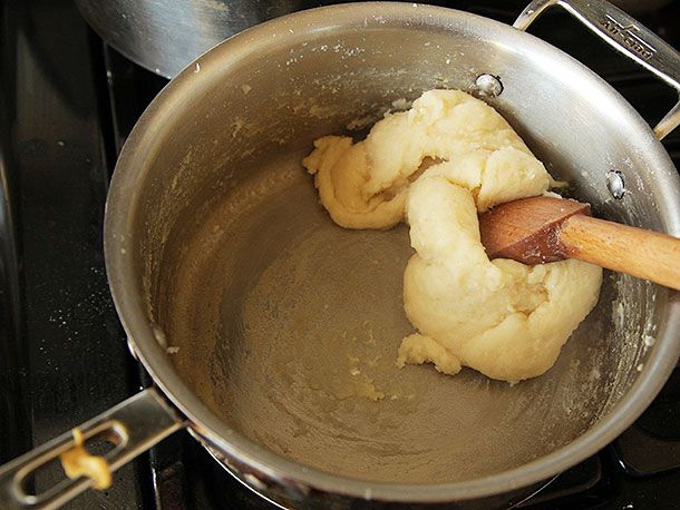 Dough being stirred with a wooden spatula in a pan.