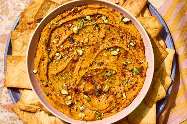 A bowl filled with a creamy zatar carrot dip garnished with chopped pistachios, accompanied by pita chips