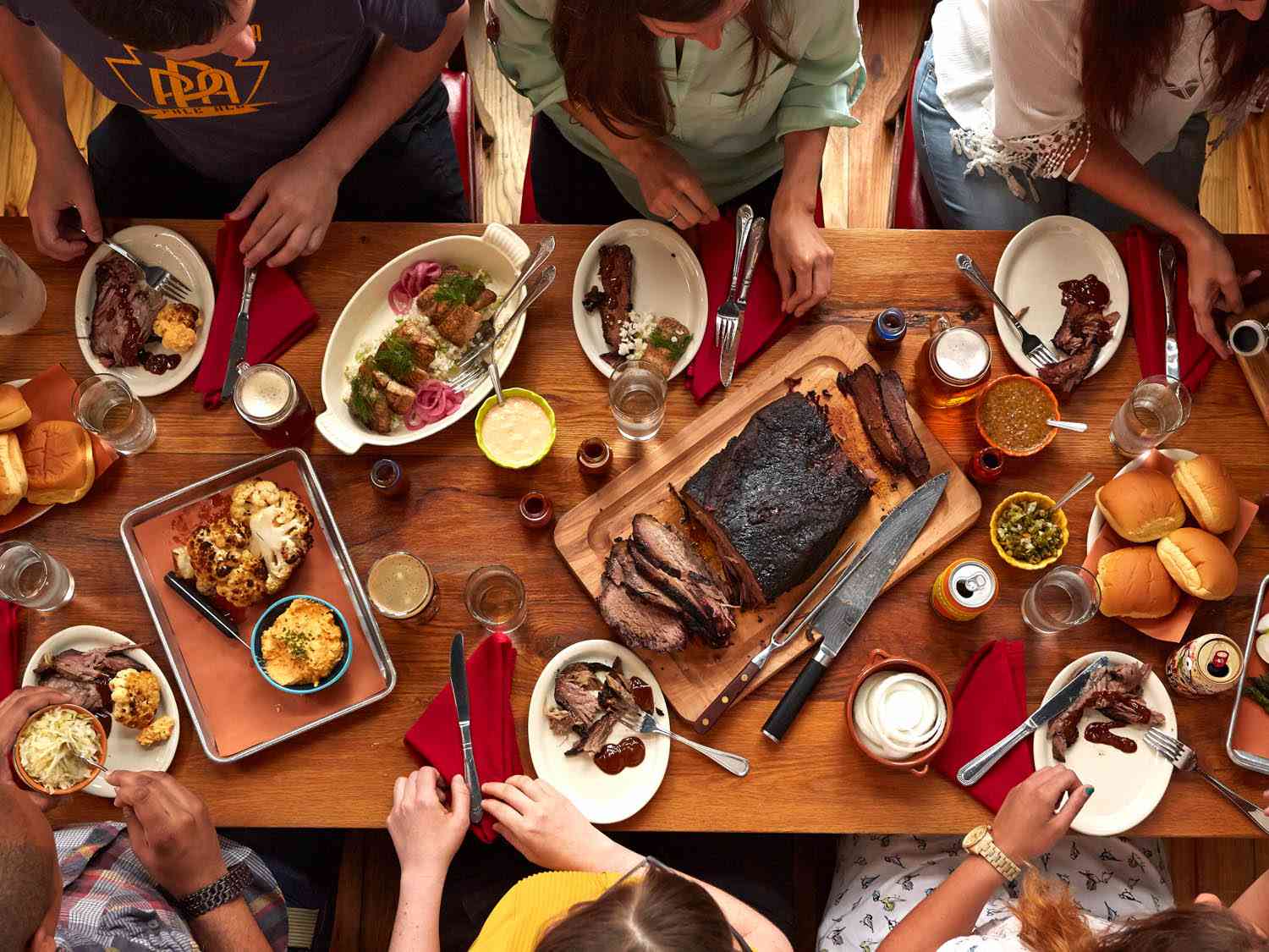 Overhead photo showing diners at a barbecue restaurant with a full table of brisket and side dishes. 