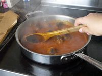 a person stirring tomato sauce with meatballs in a saute pan