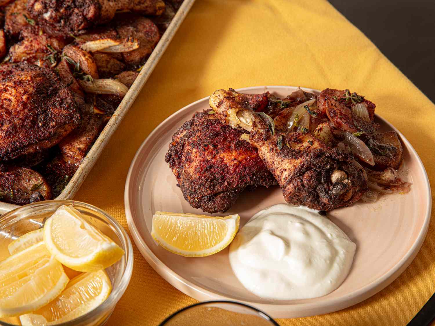 Plate with roasted chicken leg and thigh served with what seems to be yogurt sauce and lemon wedges