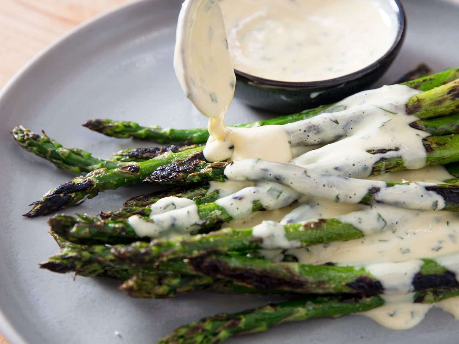 Side view of miso béarnaise being spooned over charred asparagus.