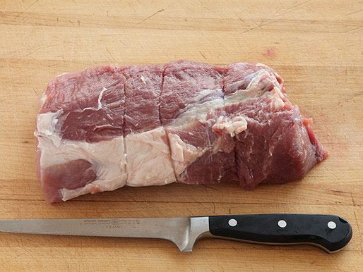 Uncooked pork sirloin on a wooden surface beside a boning knife