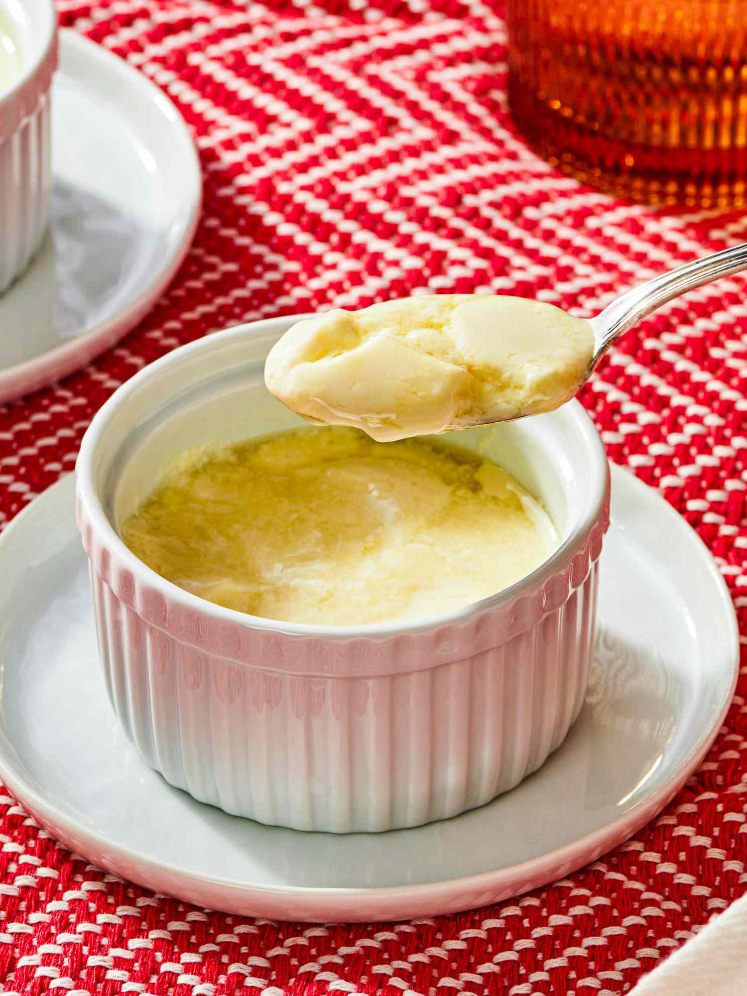 A spoonful of pudding over a white ramekin on a red patterned background
