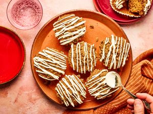 Gingerbread muffins with icing served on a plate with a hand applying more icing using a spoon