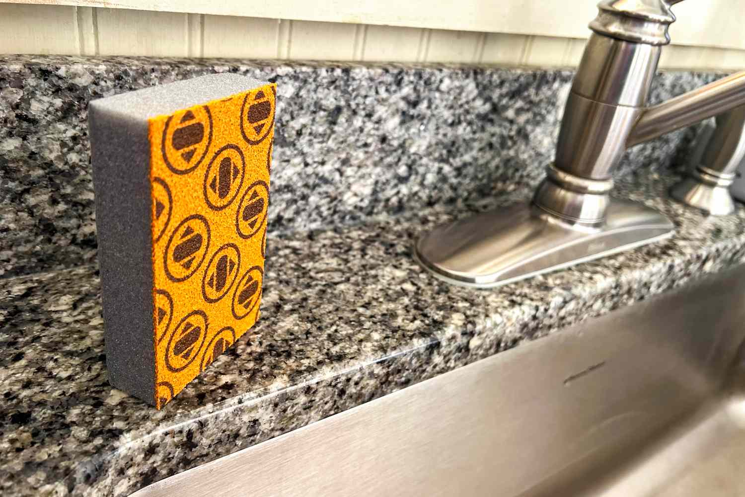 An orange Skura dishwashing sponge next to a kitchen sink