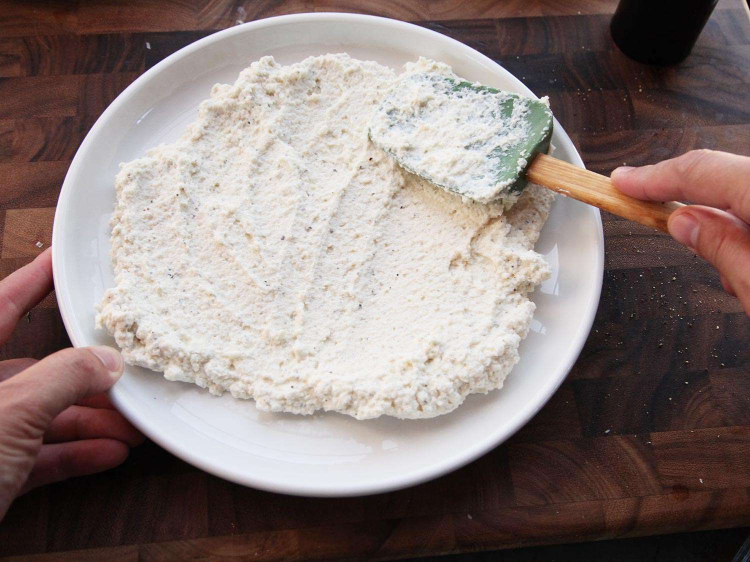 Spreading ricotta and Parmesan cheese mixture on a plate, prepared to be chilled. 