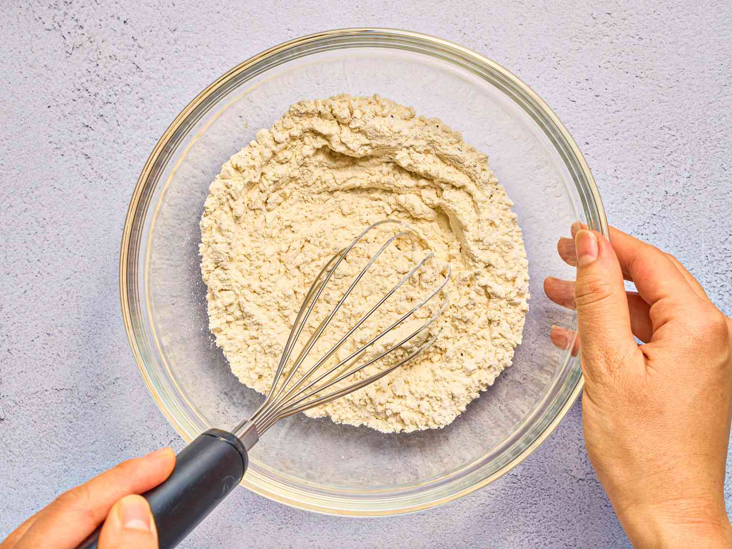 whisking together ingredients in glass bowl on stone surface