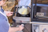 A person melting butter in a pan on the side stove of the Weber Spirit EP-435 Gas Grill