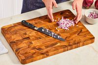 A person chopping red onion on a wooden cutting board