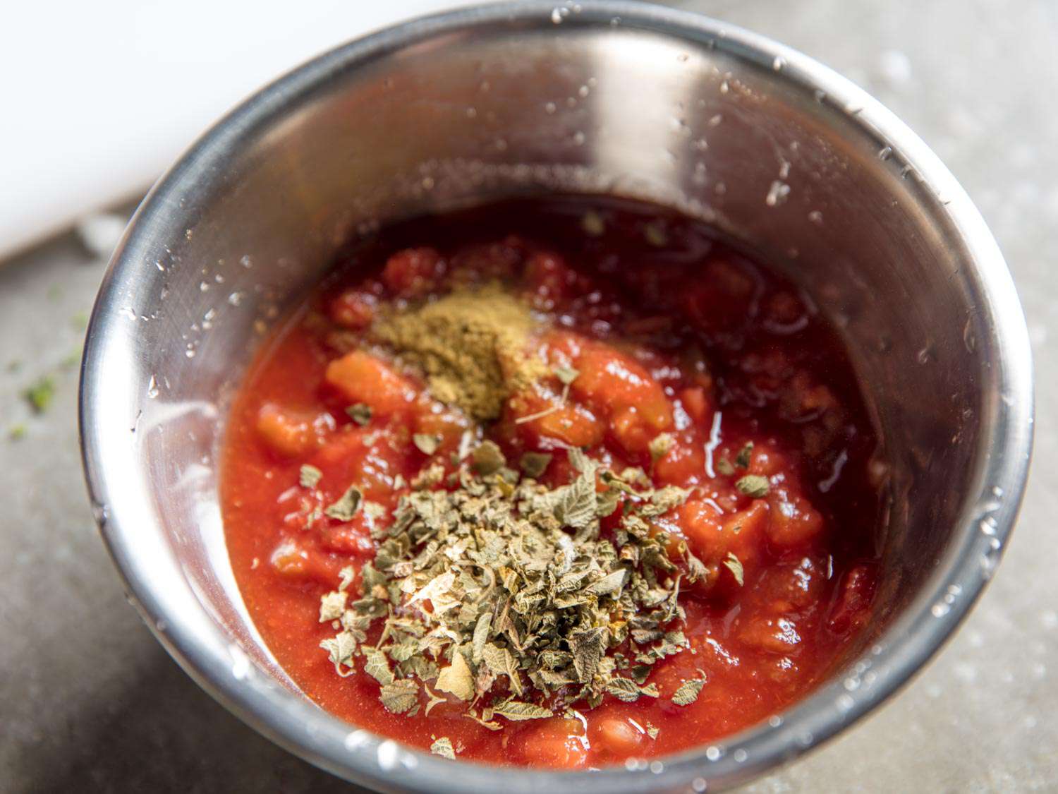 Cumin and Mexican oregano have been added to a bowl of salsa.