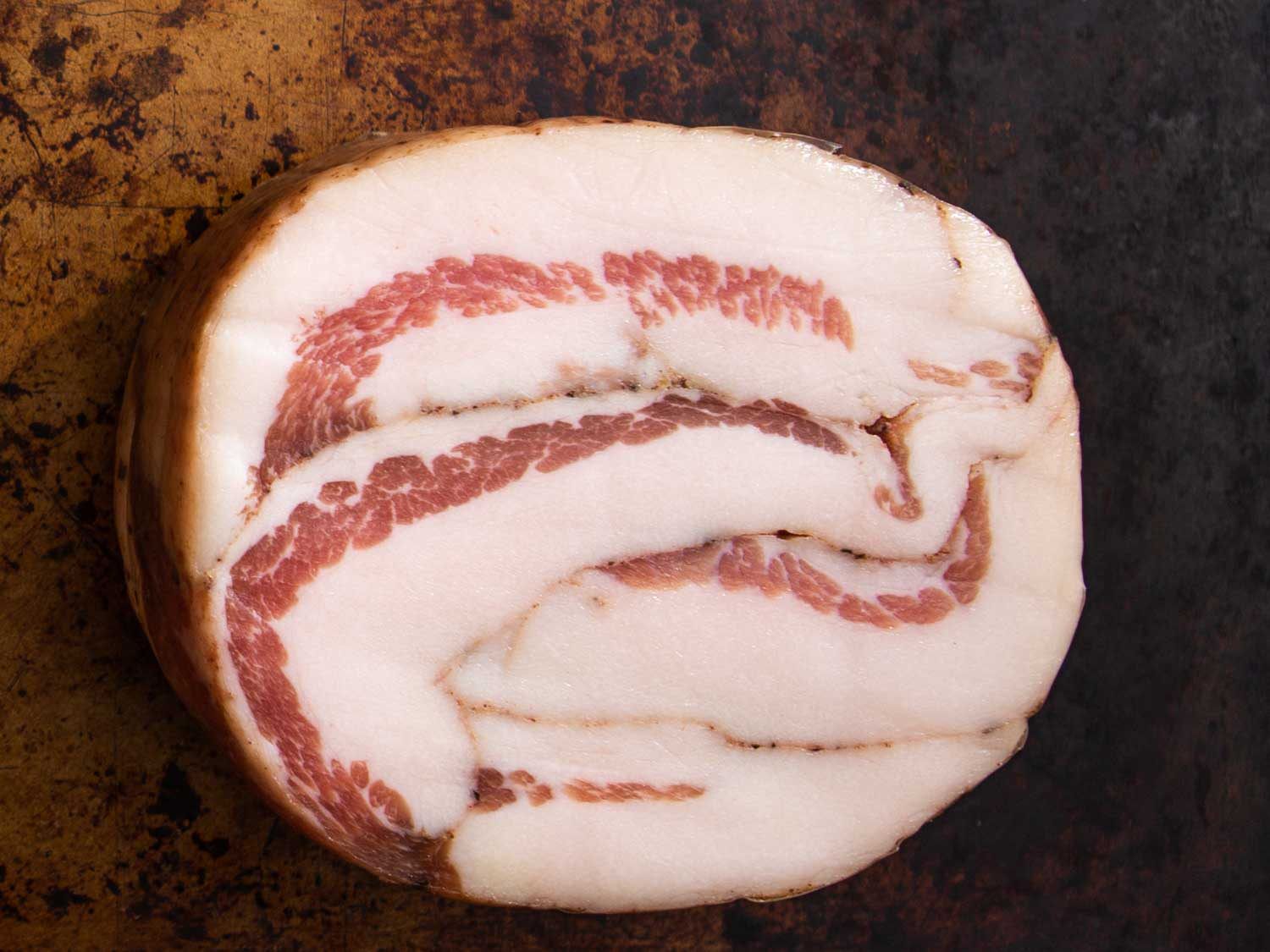 Slab of guanciale on a dark brown background.