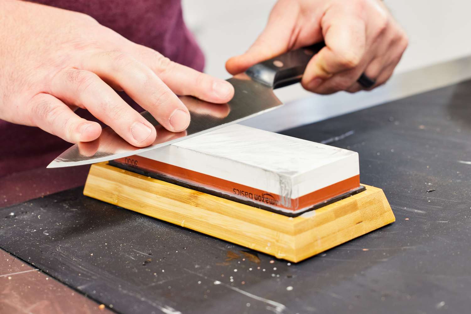 A person sharpens a knife on an Amazon Basics whetstone.