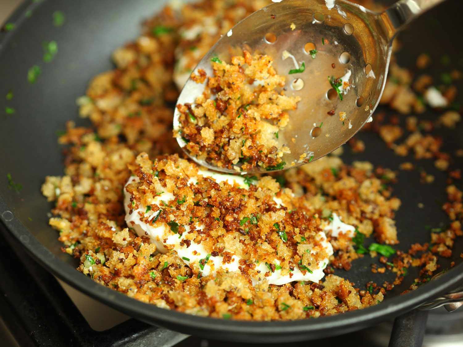 Closeup of a poached egg being coated with seasoned fried breadcrumbs.