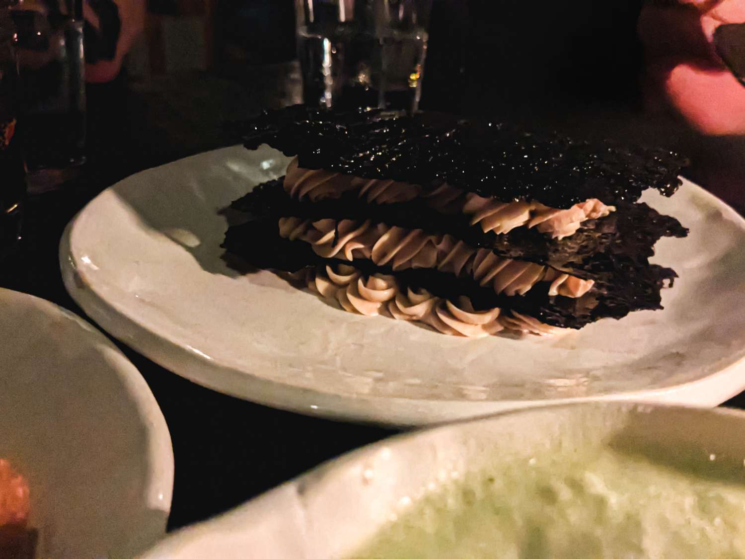 Elaborate dessert on a plate featuring stacked components and piped cream set on a dining table